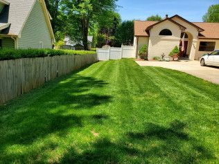 A lush green lawn in front of a house with a white car parked in the driveway.