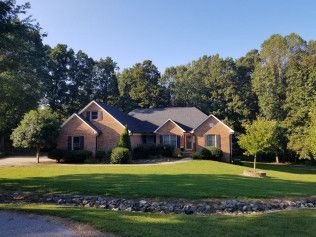 A large brick house with a lush green lawn and trees in the background
