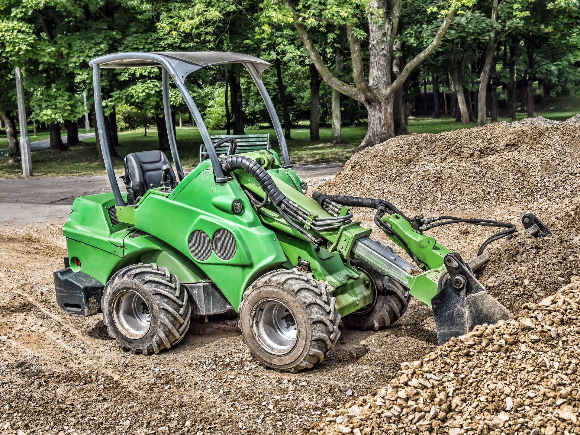 A green tractor is driving through a pile of gravel.