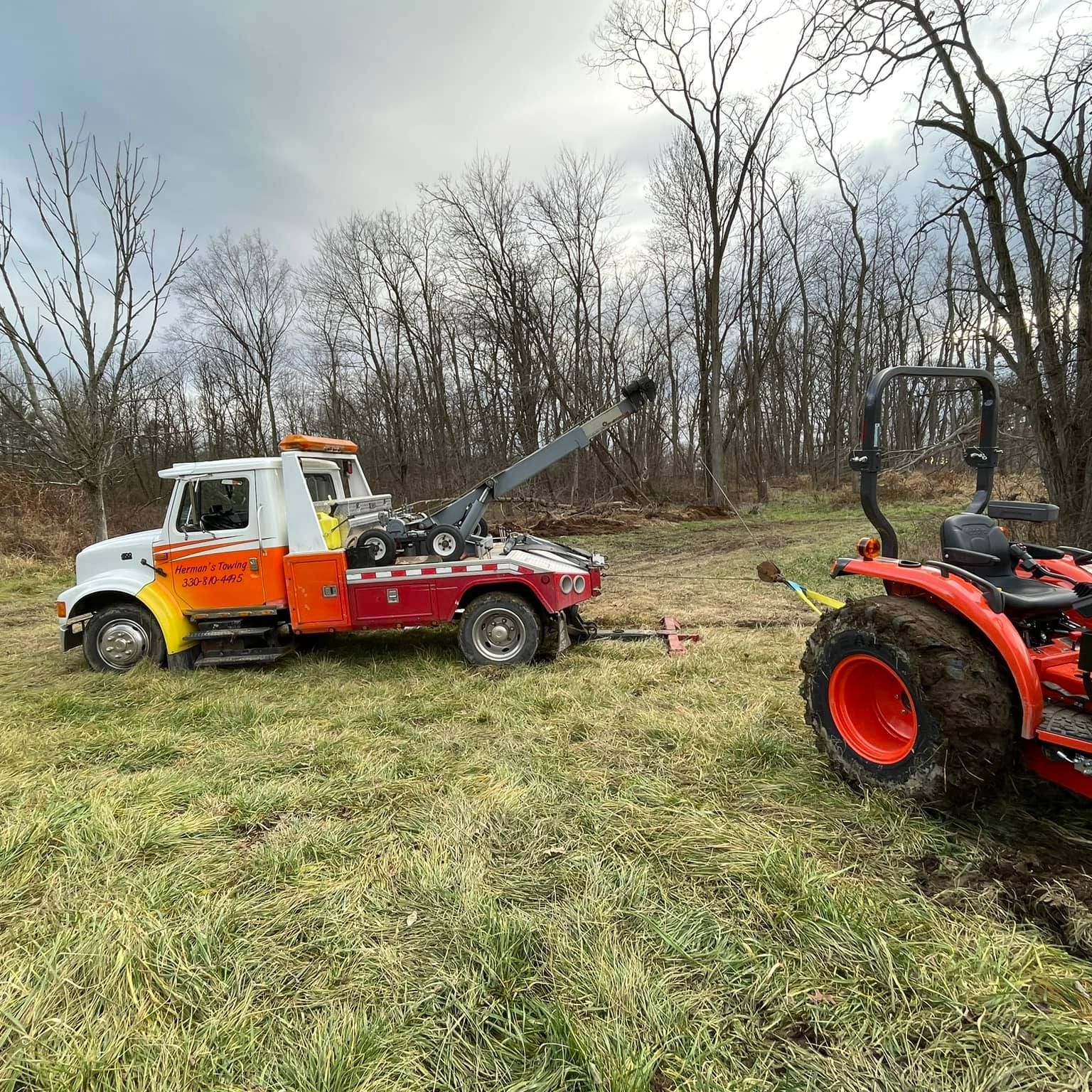 A tow truck is towing a tractor in a field.