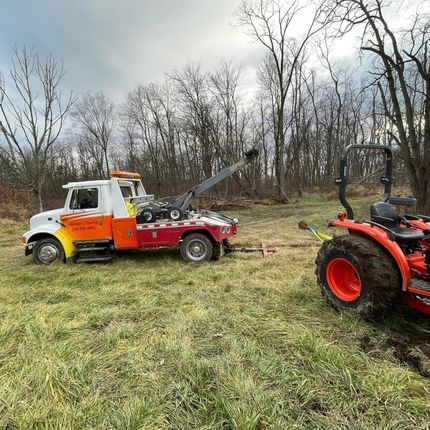 A tow truck is towing a tractor in a field.
