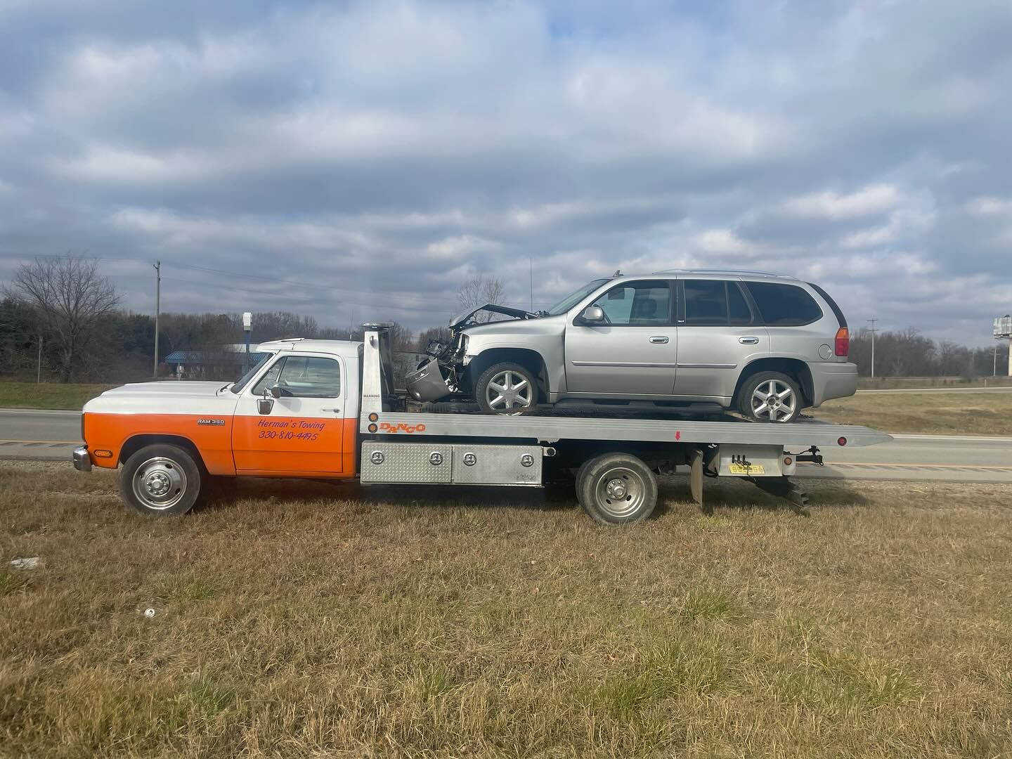 A tow truck is carrying a silver suv on the back of it.
