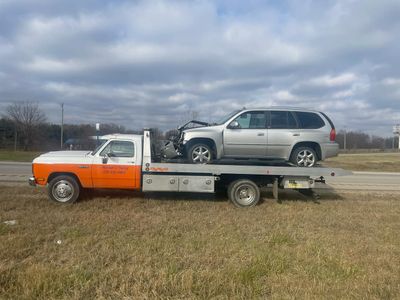 A tow truck is carrying a silver suv on the back of it.