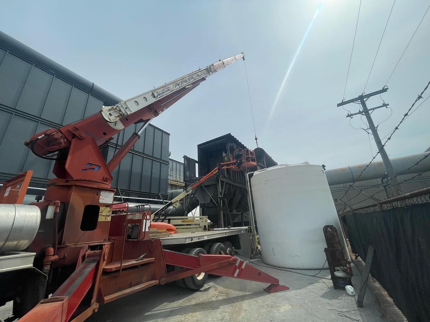 A red crane is parked next to a white tank.