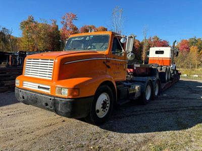 Orange semi-truck hauling a white and orange truck on a flatbed trailer, parked outdoors on a sunny day.