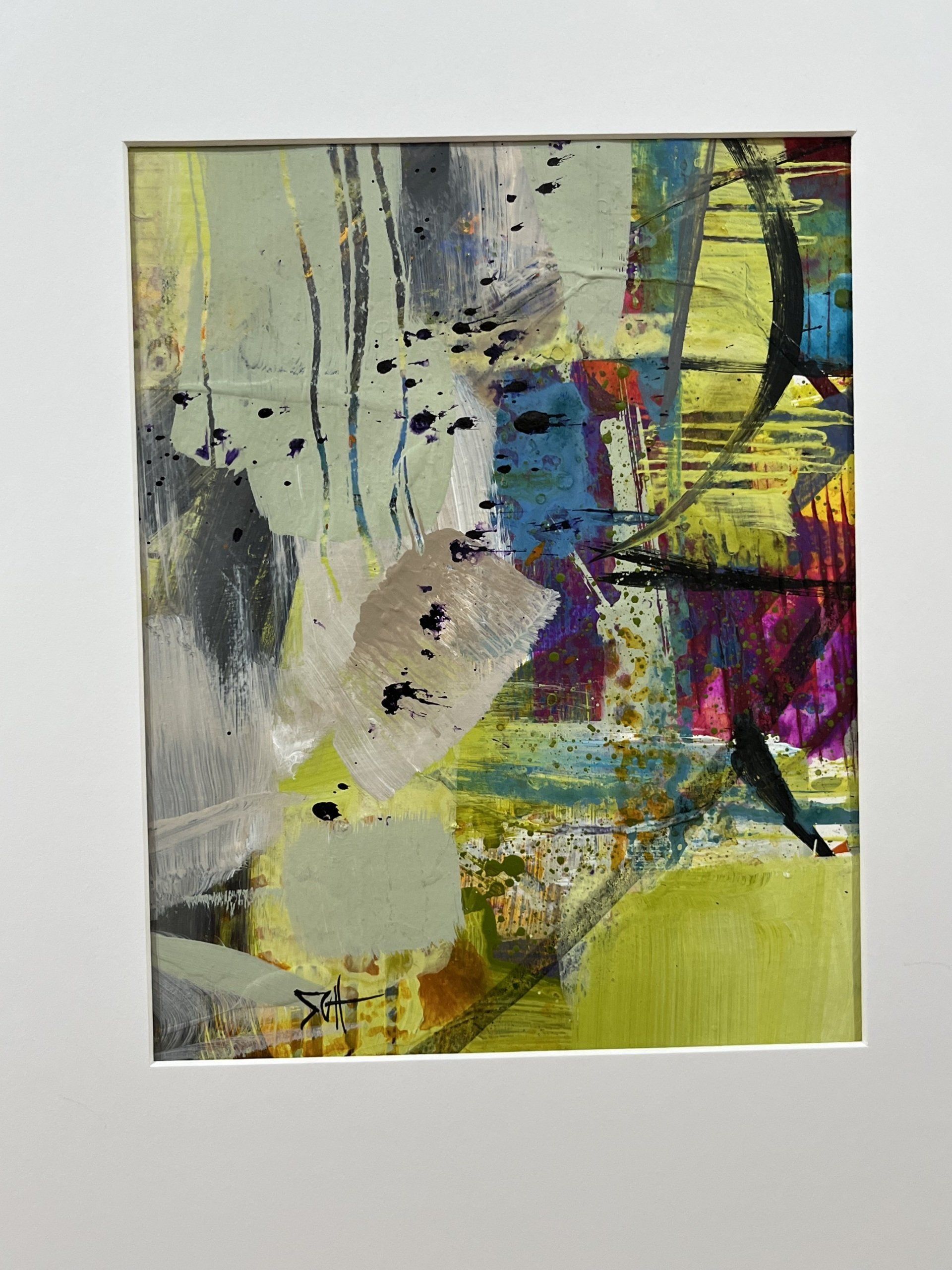 A colorful abstract painting is framed in a white frame