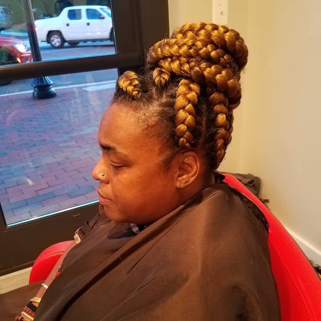 Woman with golden braided hair styled in a high bun, seated near a window.