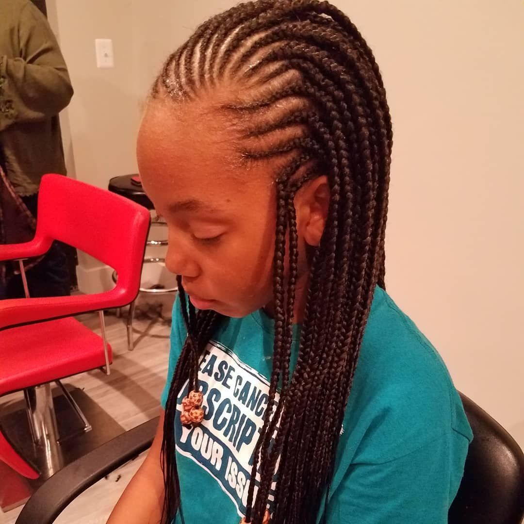 Girl with long, braided hair, wearing a teal shirt, sitting in a salon chair.