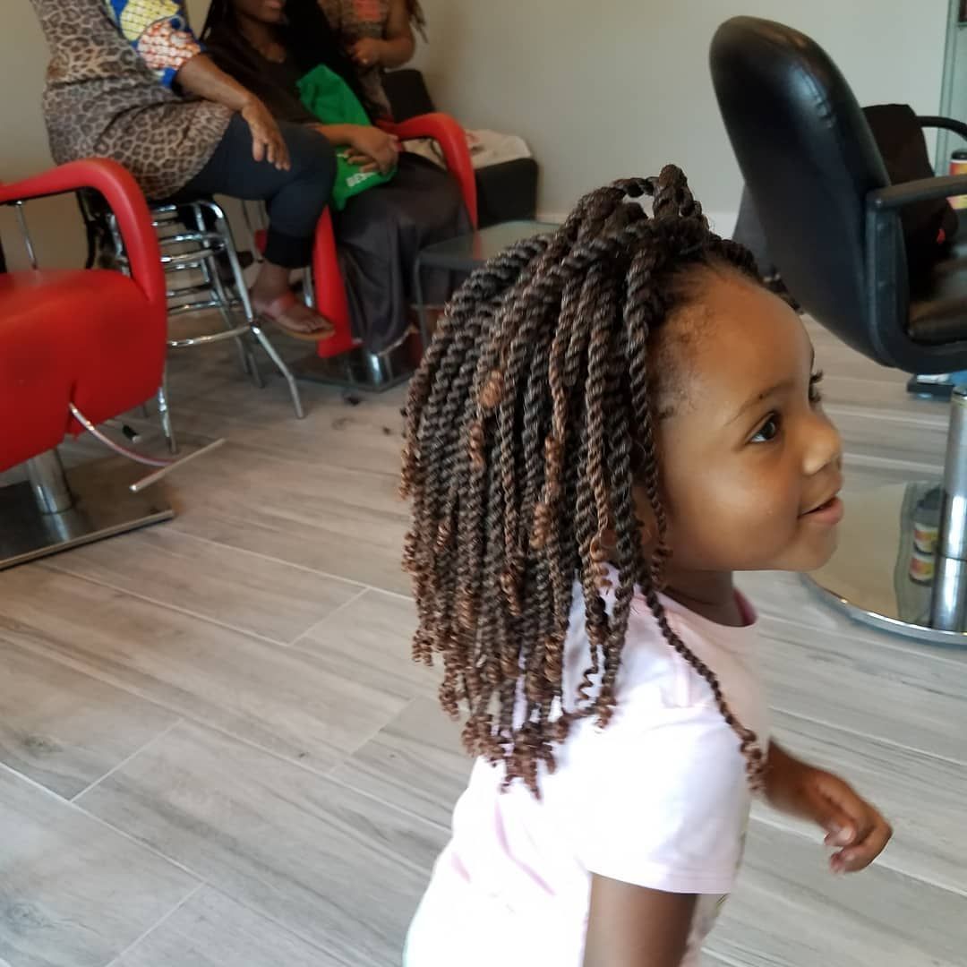Young child with brown twists smiles, standing in a hair salon.