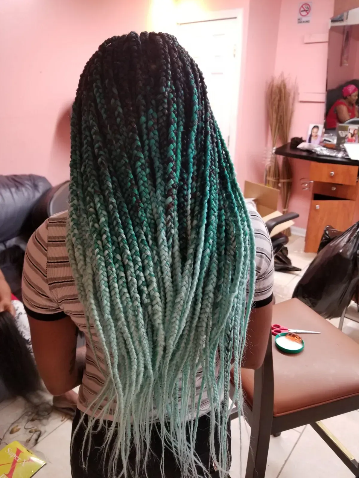Woman with long, ombre braids in shades of teal and black, standing inside a salon.