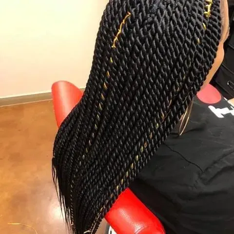 Black rope twists hairstyle with gold accents, resting on a red chair.