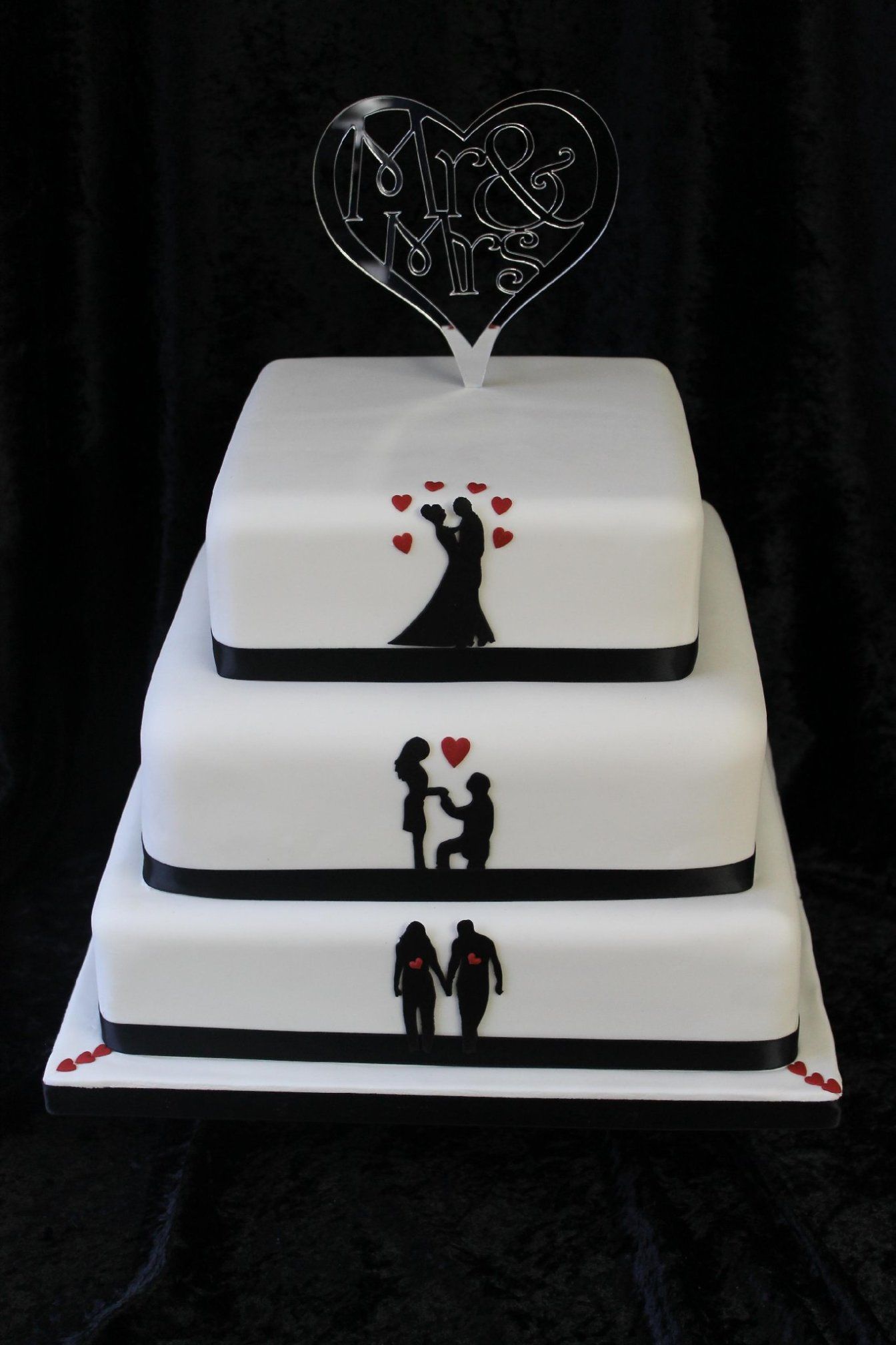 A three tier square wedding cake with black silhouettes and red love hearts on it. .