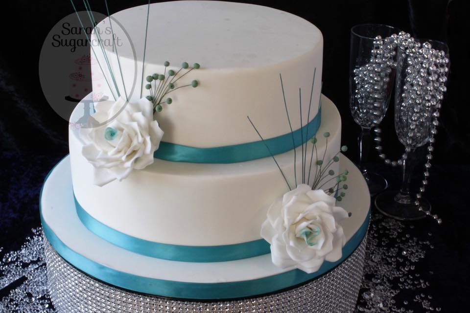 A stunning white wedding cake with teal ribbons. The white sugar flowers also have teal accents.