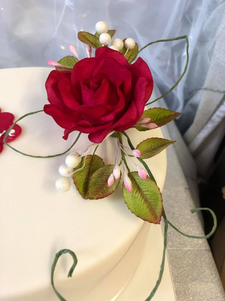 A close-up of a red rose on top of a white wedding cake