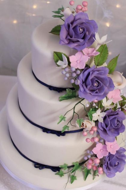 A 4-tier wedding cake with purple and pink sugar flowers running down one side.