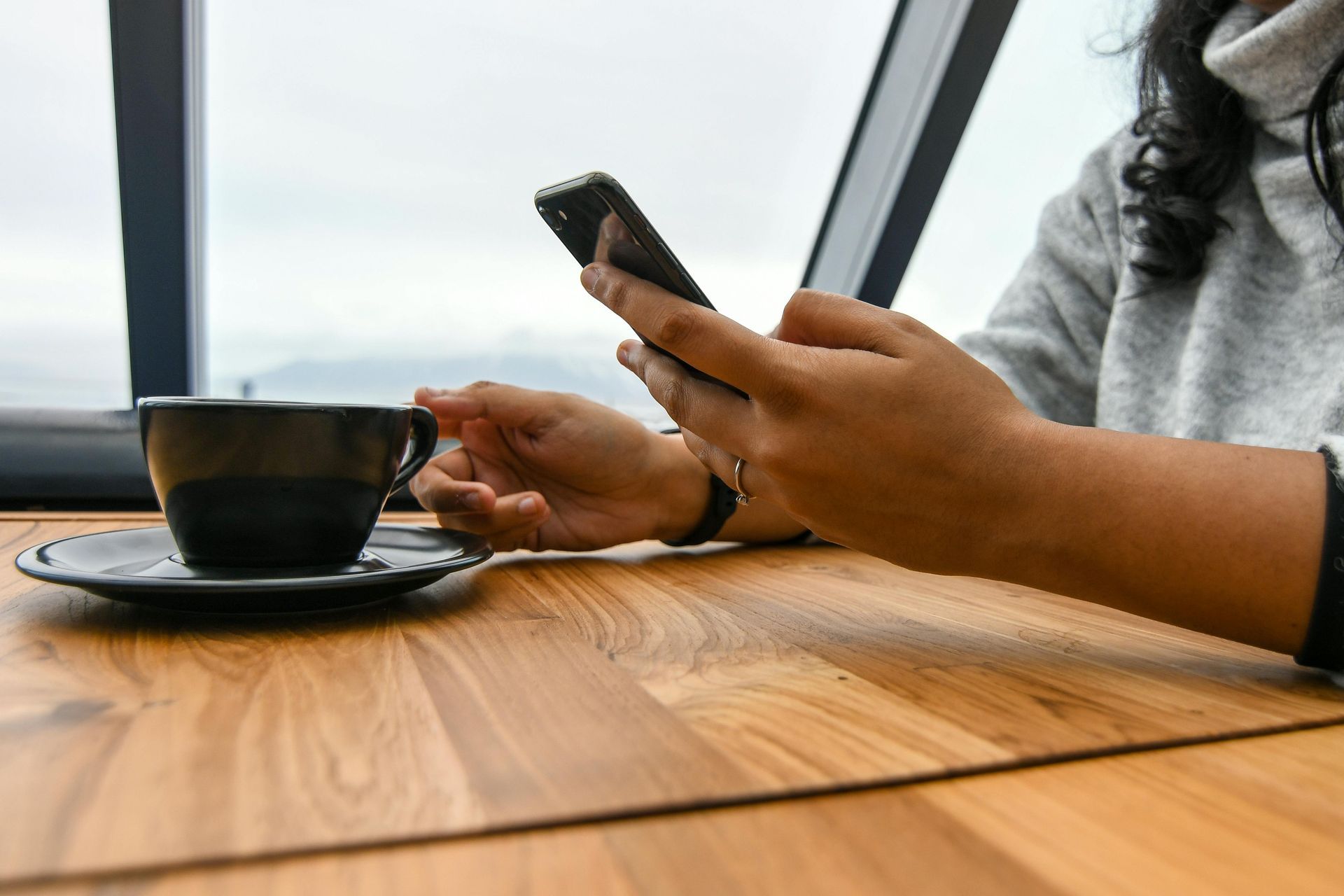 A woman is sitting at a table with a cup of coffee and a cell phone.