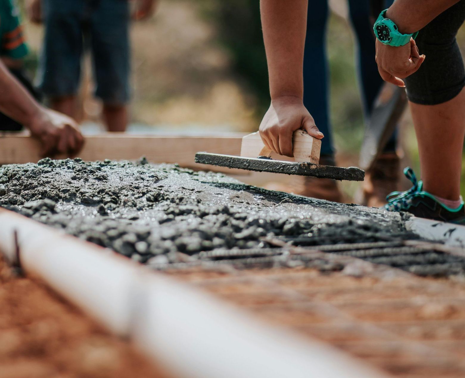 A person is spreading concrete on the ground with a trowel.