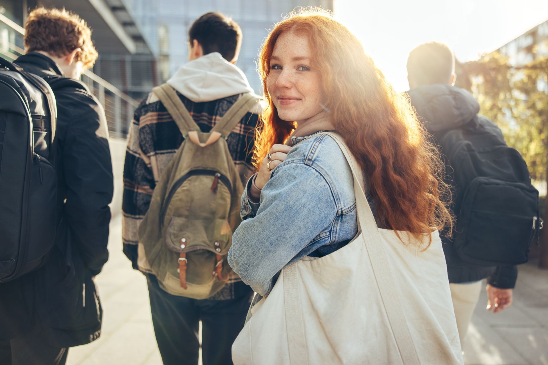 A young woman with long red hair smiles at the camera while walking with friends.