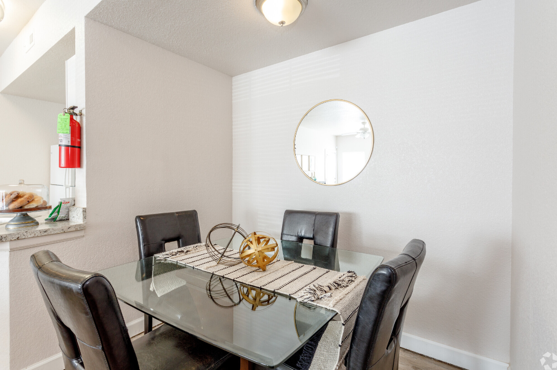 Dining room with glass table, black chairs, and round mirror.