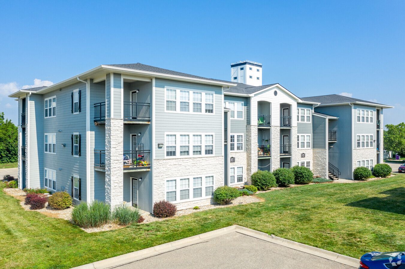 Blue and white apartment building with balconies on a sunny day. Green grass and blue sky.