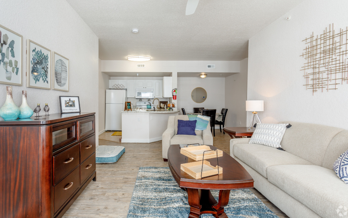 Cozy living room with a sofa, rug, and wooden coffee table leading to a kitchen and dining area.