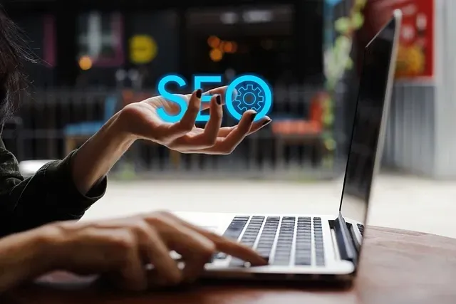 A woman is using a laptop computer and holding up a sign that says SEO.