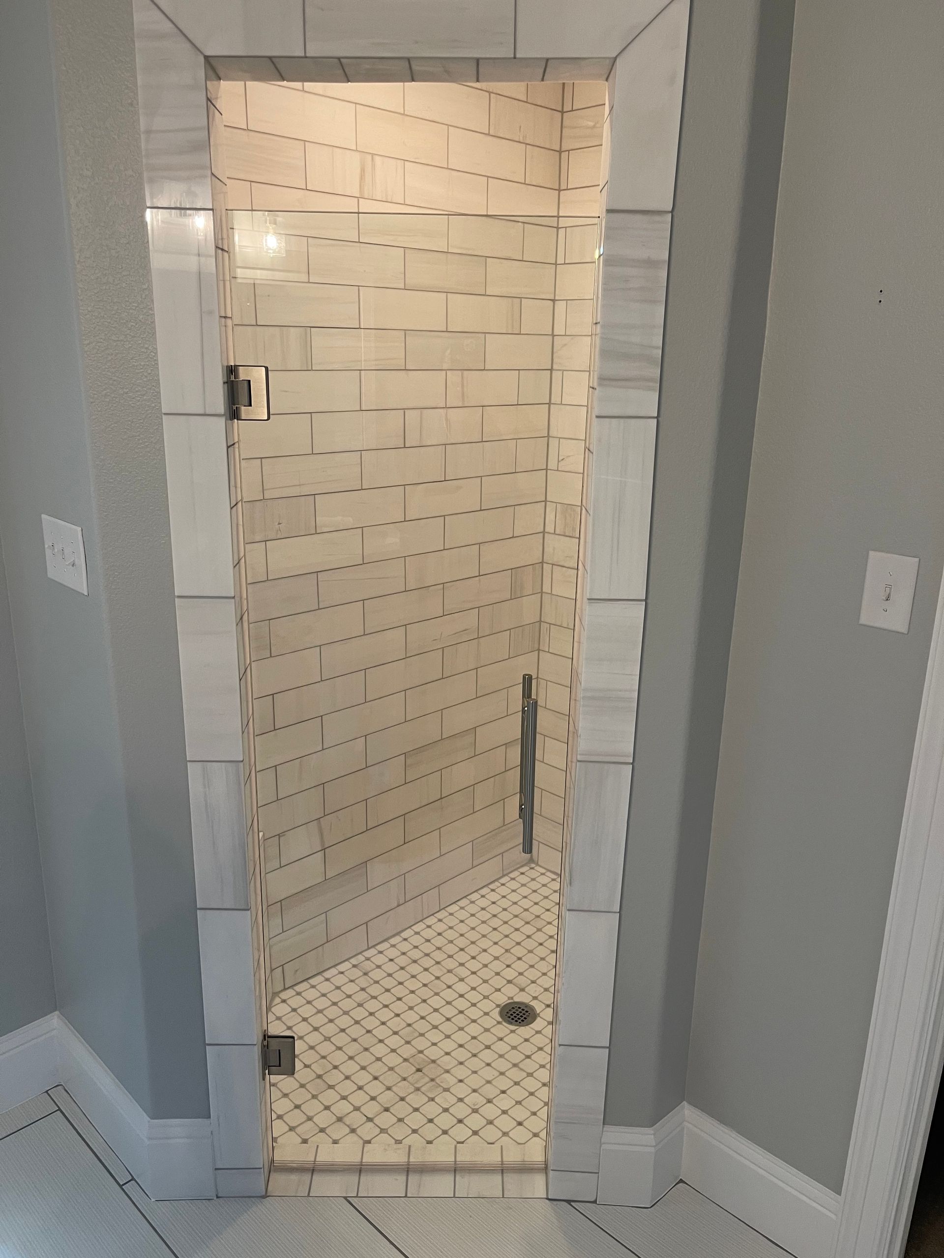 Tiled shower stall with white and gray tiles, glass door, and a white border.