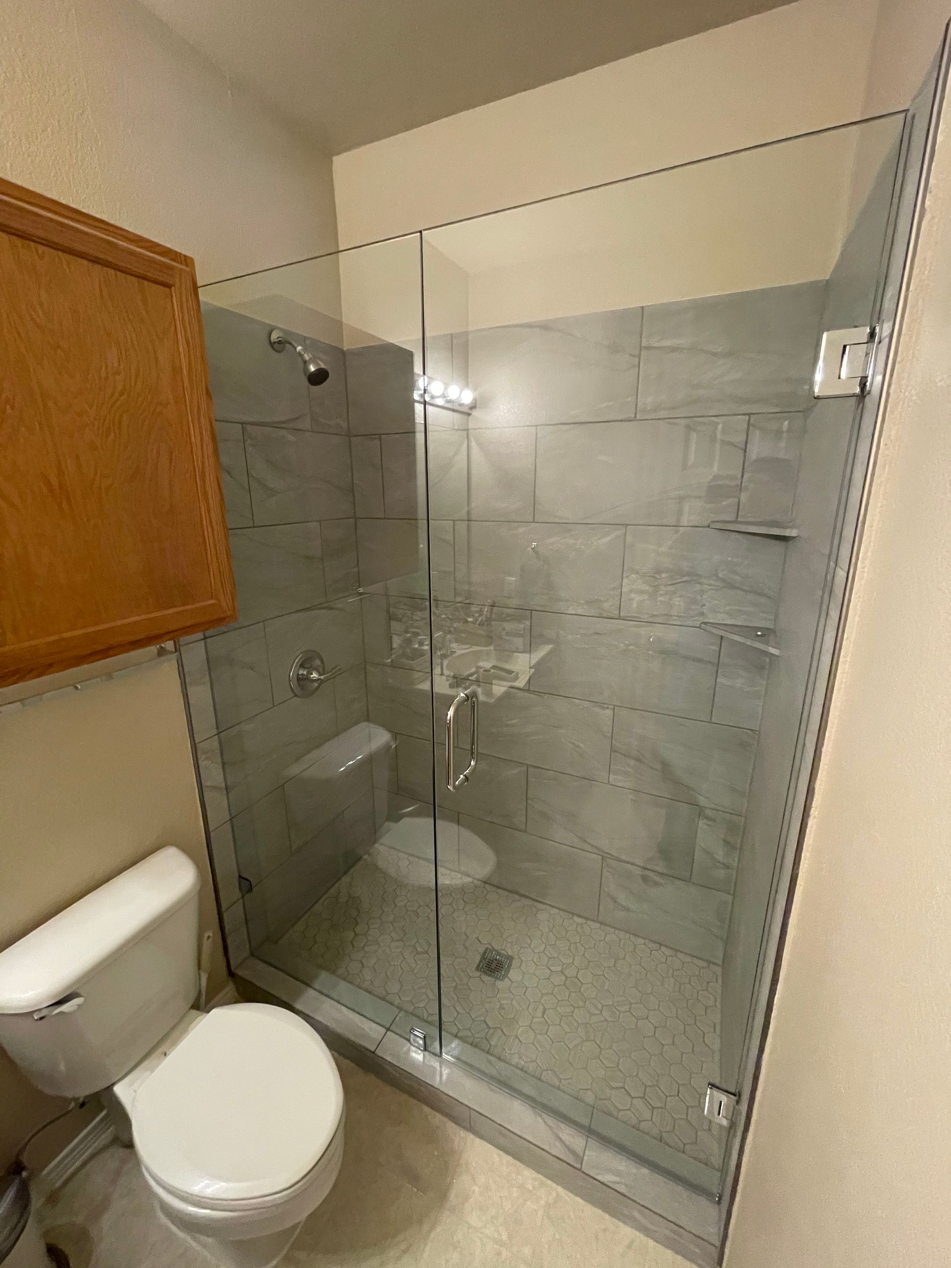Bathroom with a glass shower enclosure, gray tiled walls, and a toilet.