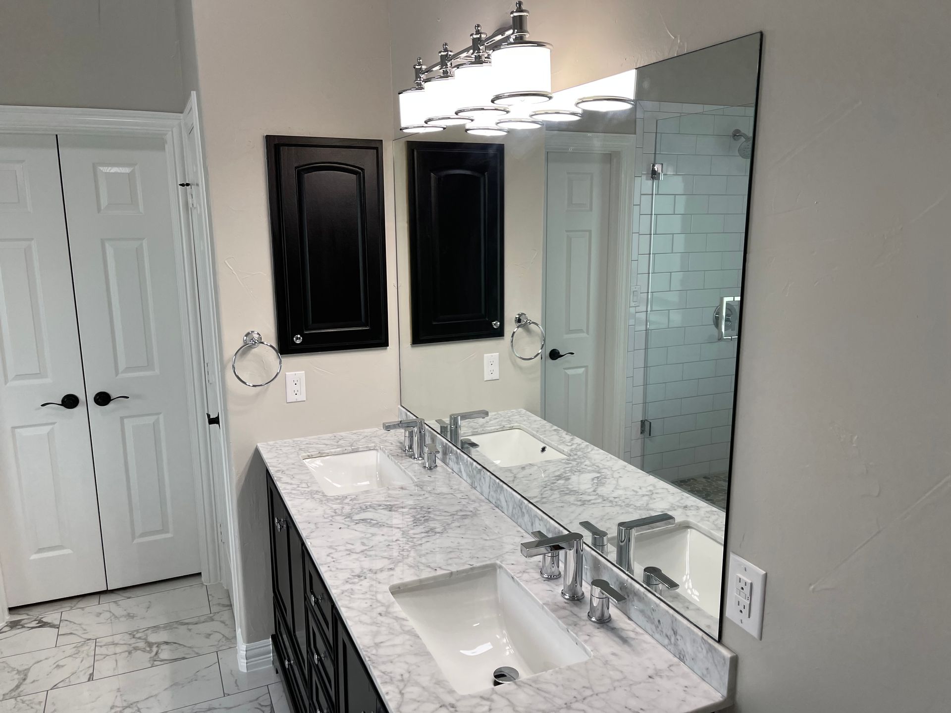 Bathroom with double sinks, large mirror, black cabinets, and white countertop.