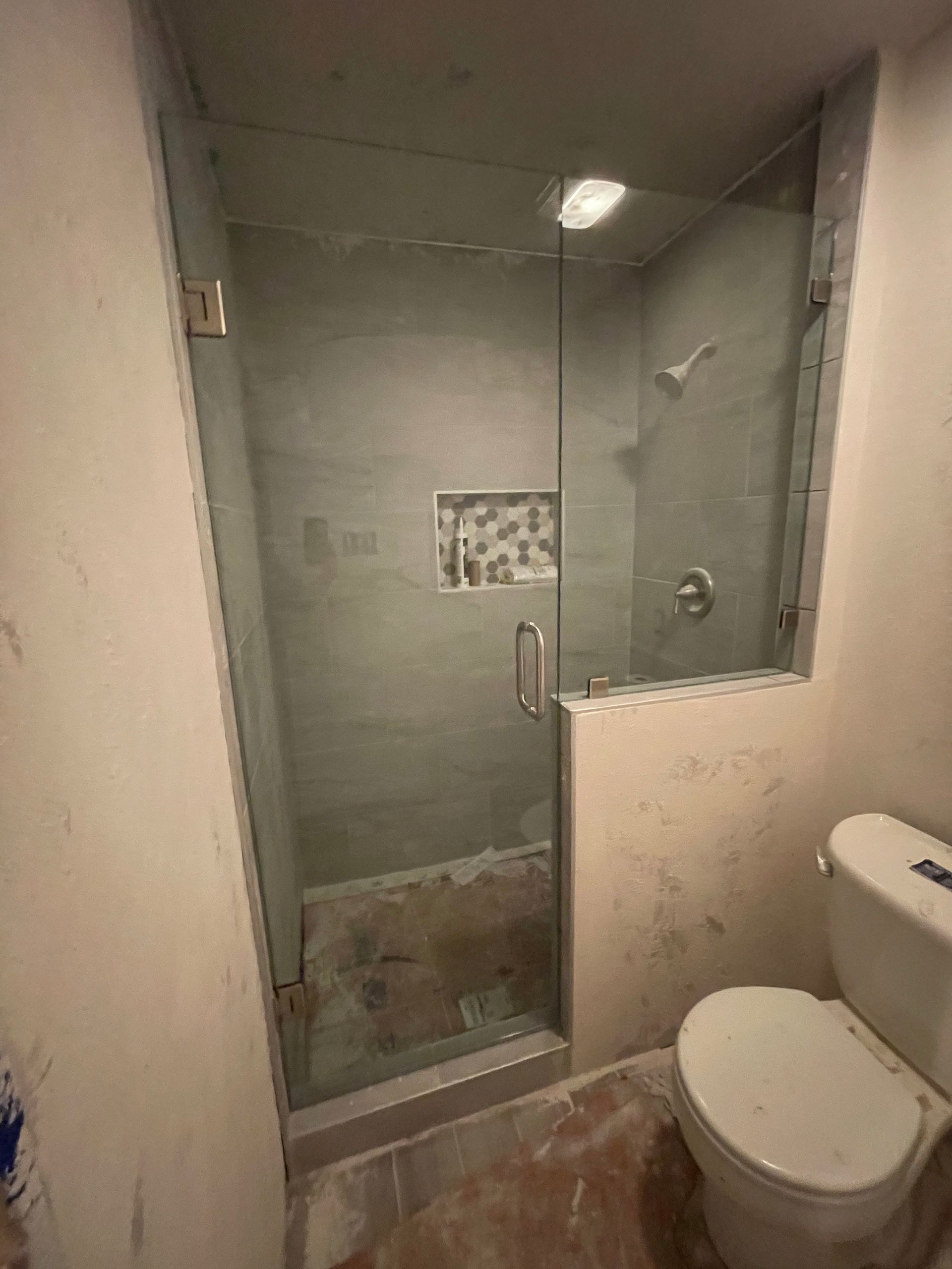 Bathroom with glass shower door, gray tiled walls, toilet, and shower fixtures.