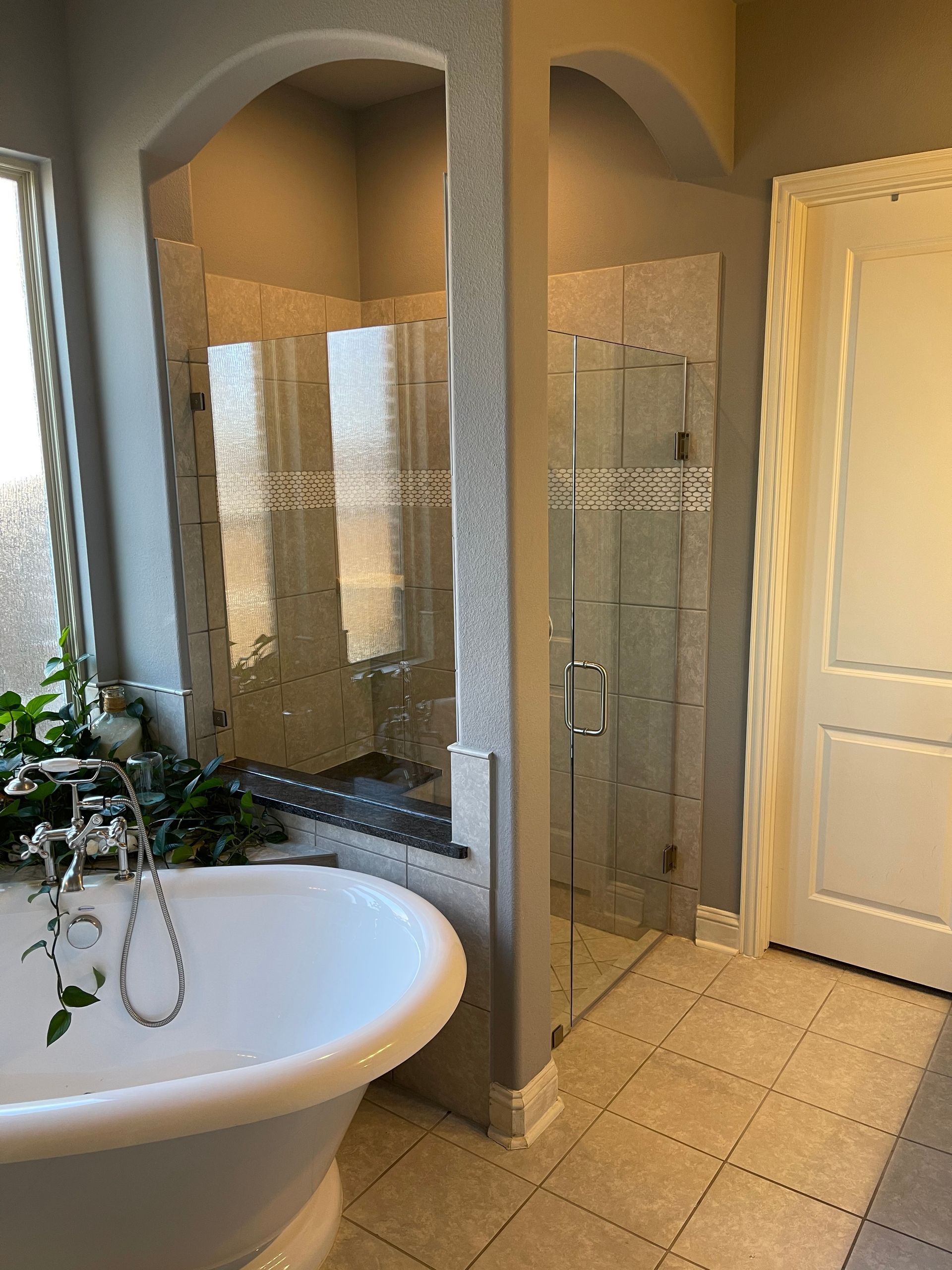 Bathroom with a white claw-foot tub, glass shower, tile floor, and a white door.