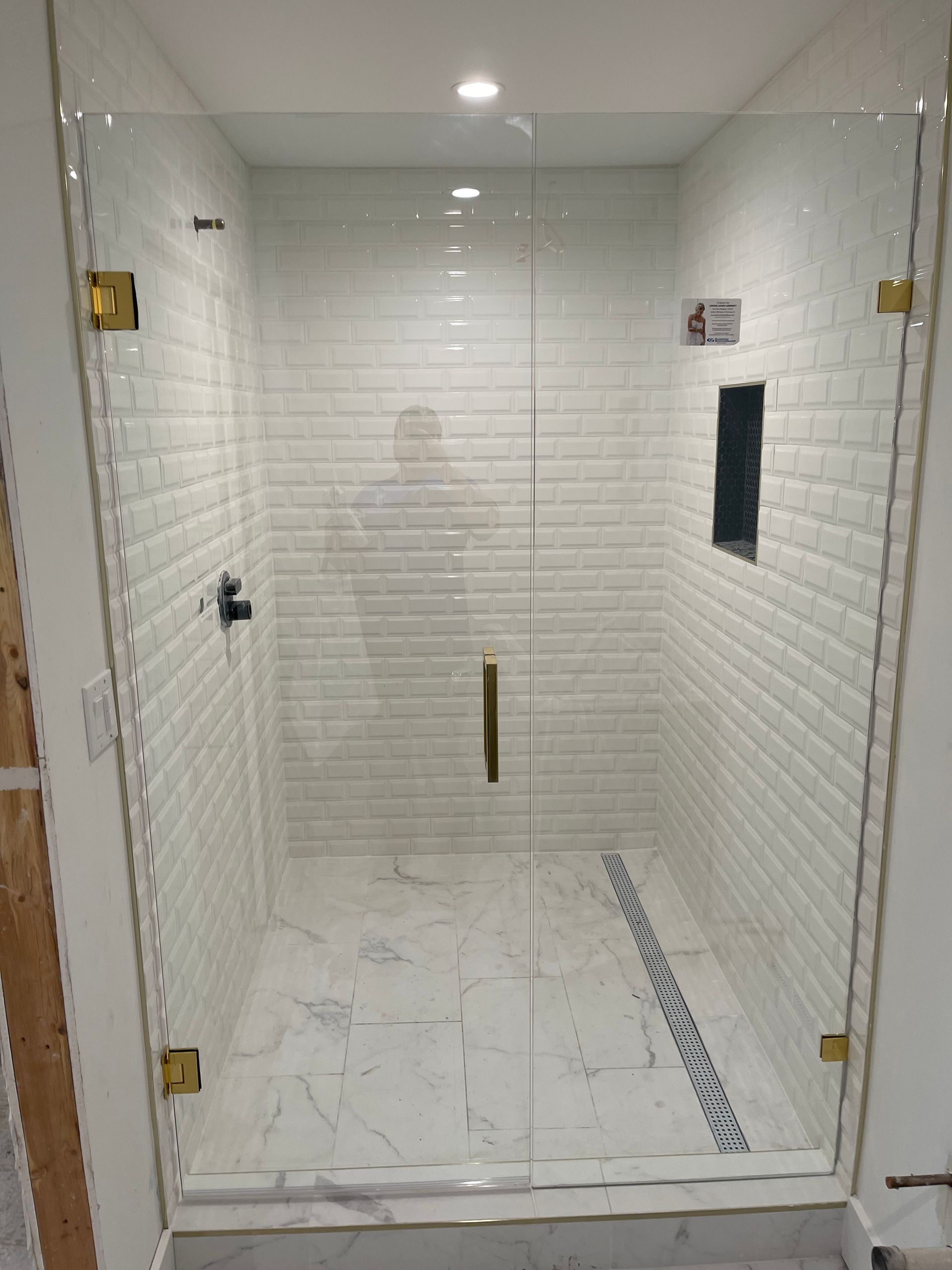 Glass shower enclosure with gold hardware, white brick tile walls and marble floor.