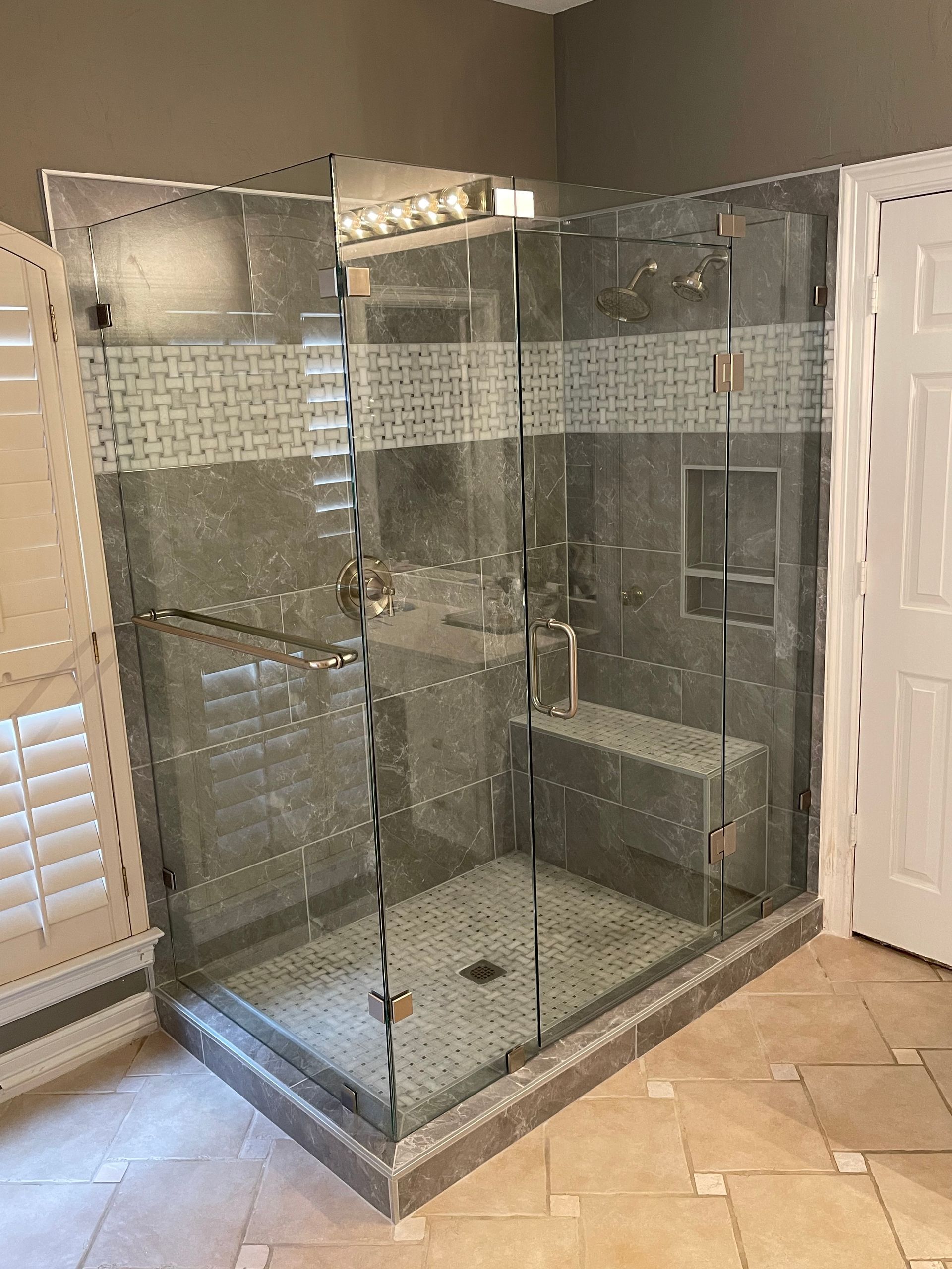 Glass shower enclosure with gray tile walls, a built-in bench, and a light-colored floor.