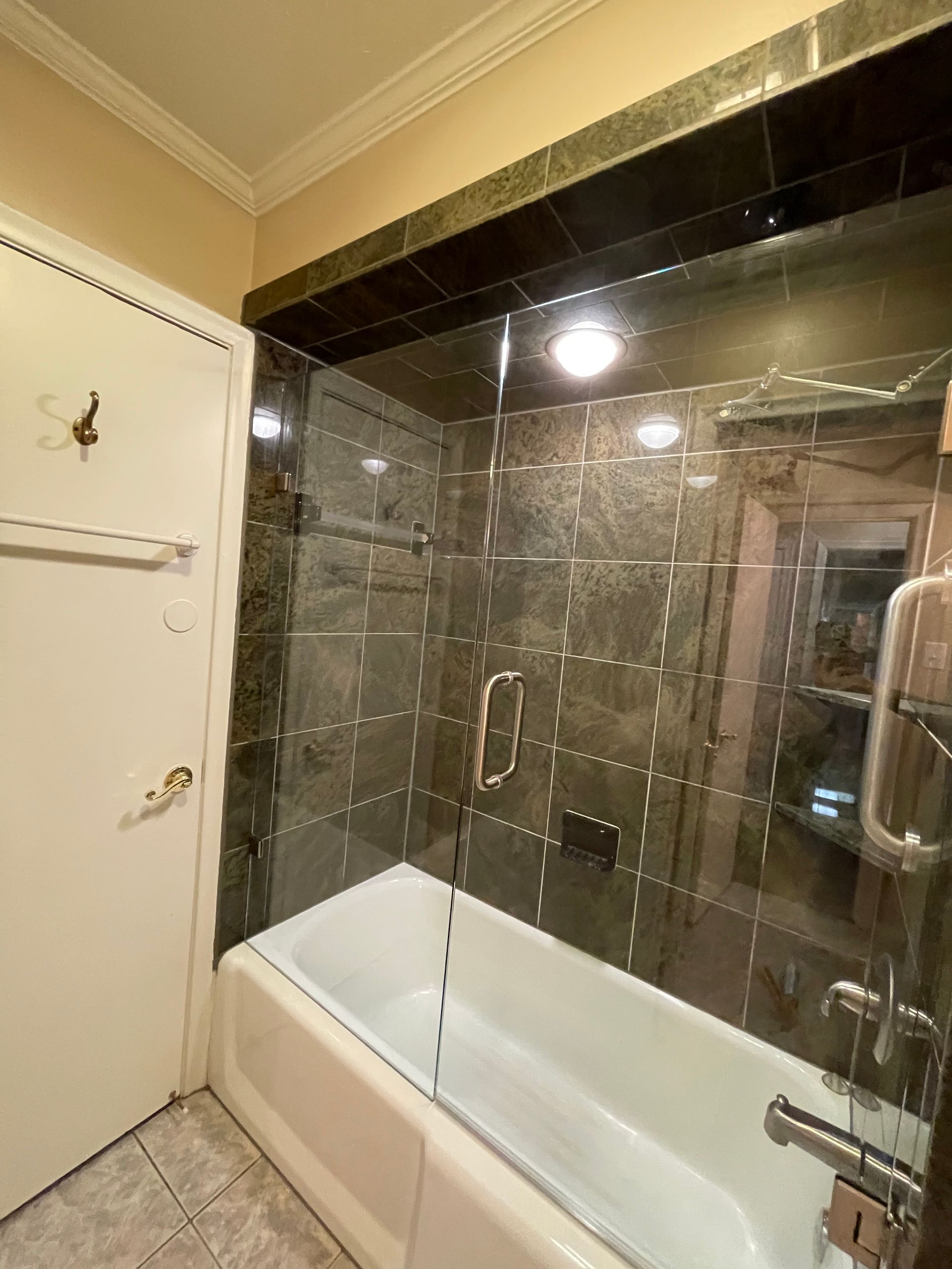 Bathroom with a white bathtub and glass shower enclosure, dark tiled walls.