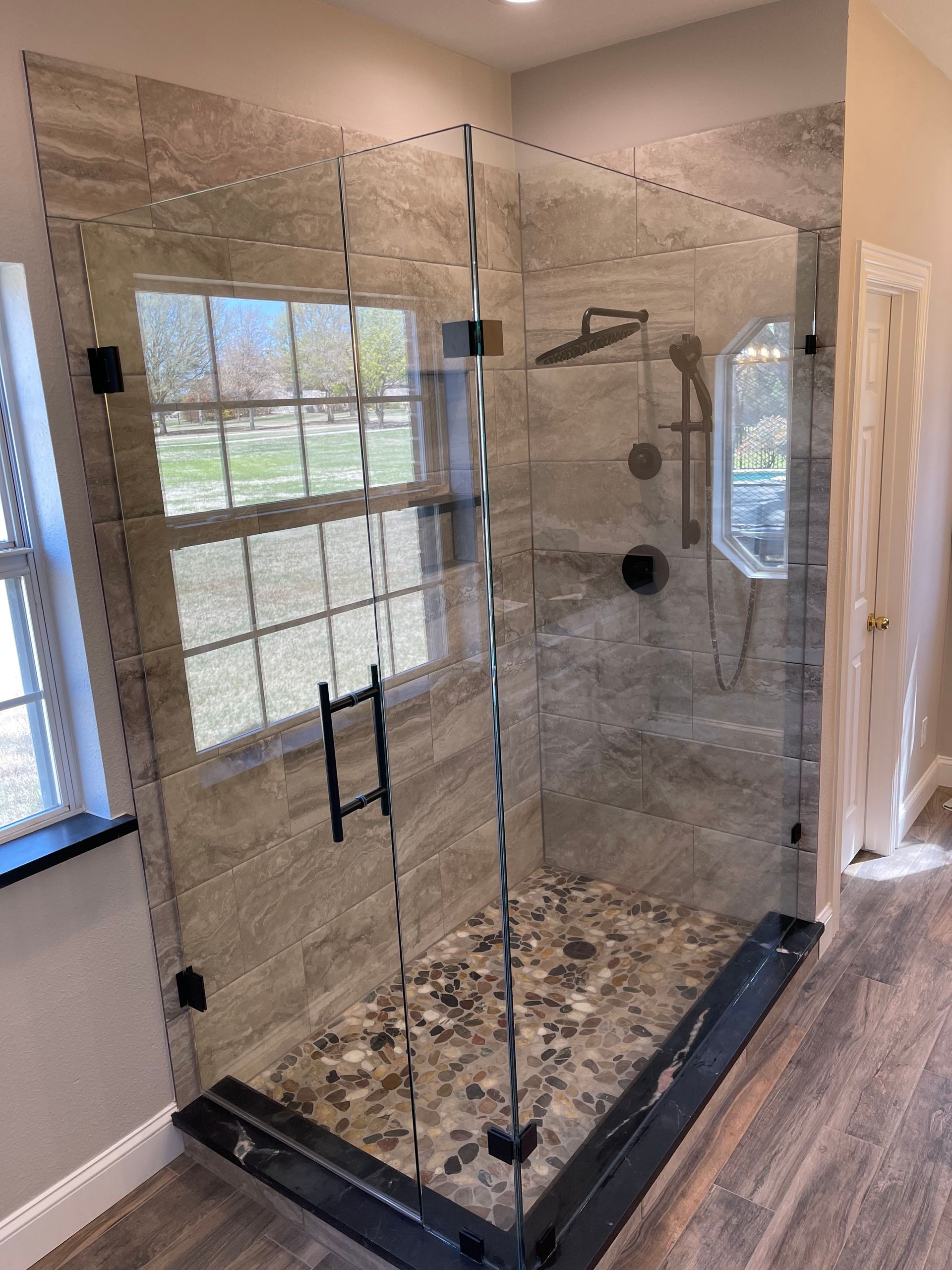 Glass shower enclosure with gray tile walls, pebble floor, and black hardware.