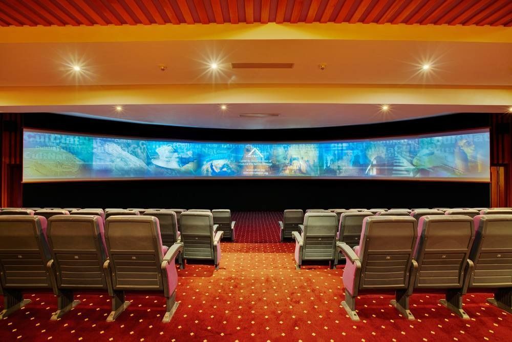 Empty movie theater with curved screen, rows of seats, red carpet.