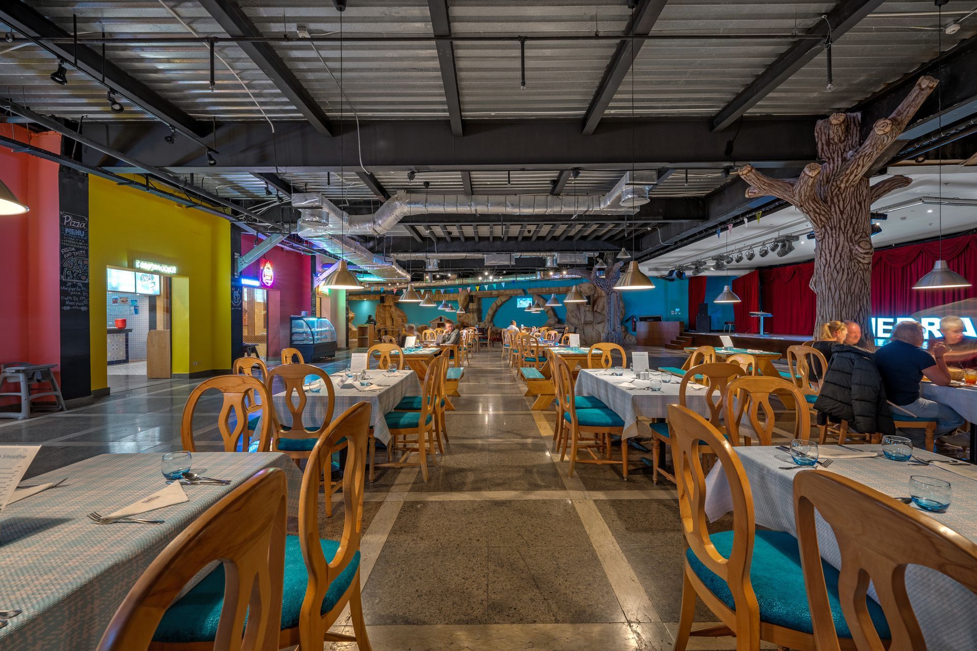 Restaurant interior with tables set, colorful walls, and overhead lighting.