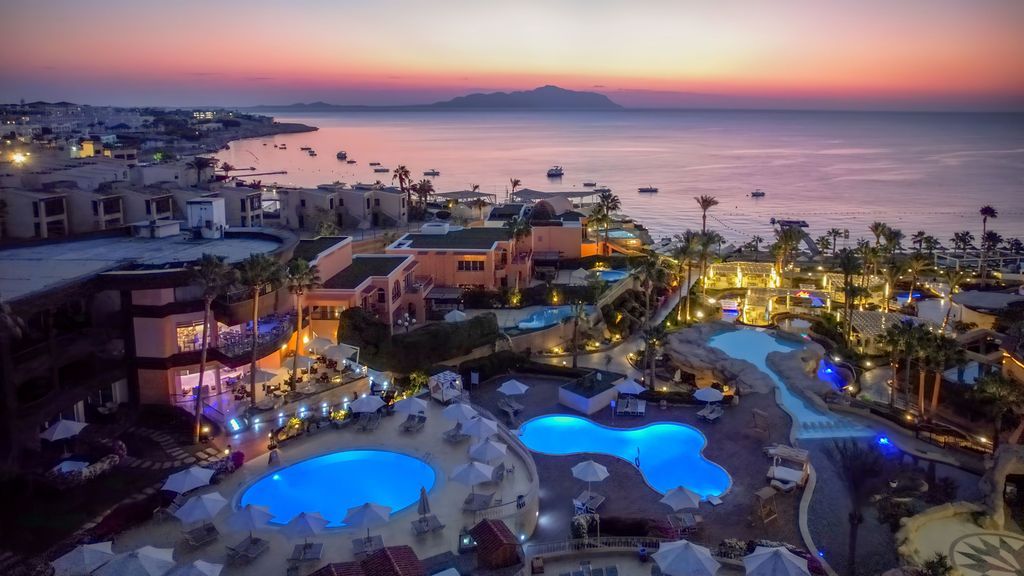 Resort at dusk with illuminated pools, ocean view, and a colorful sunset.