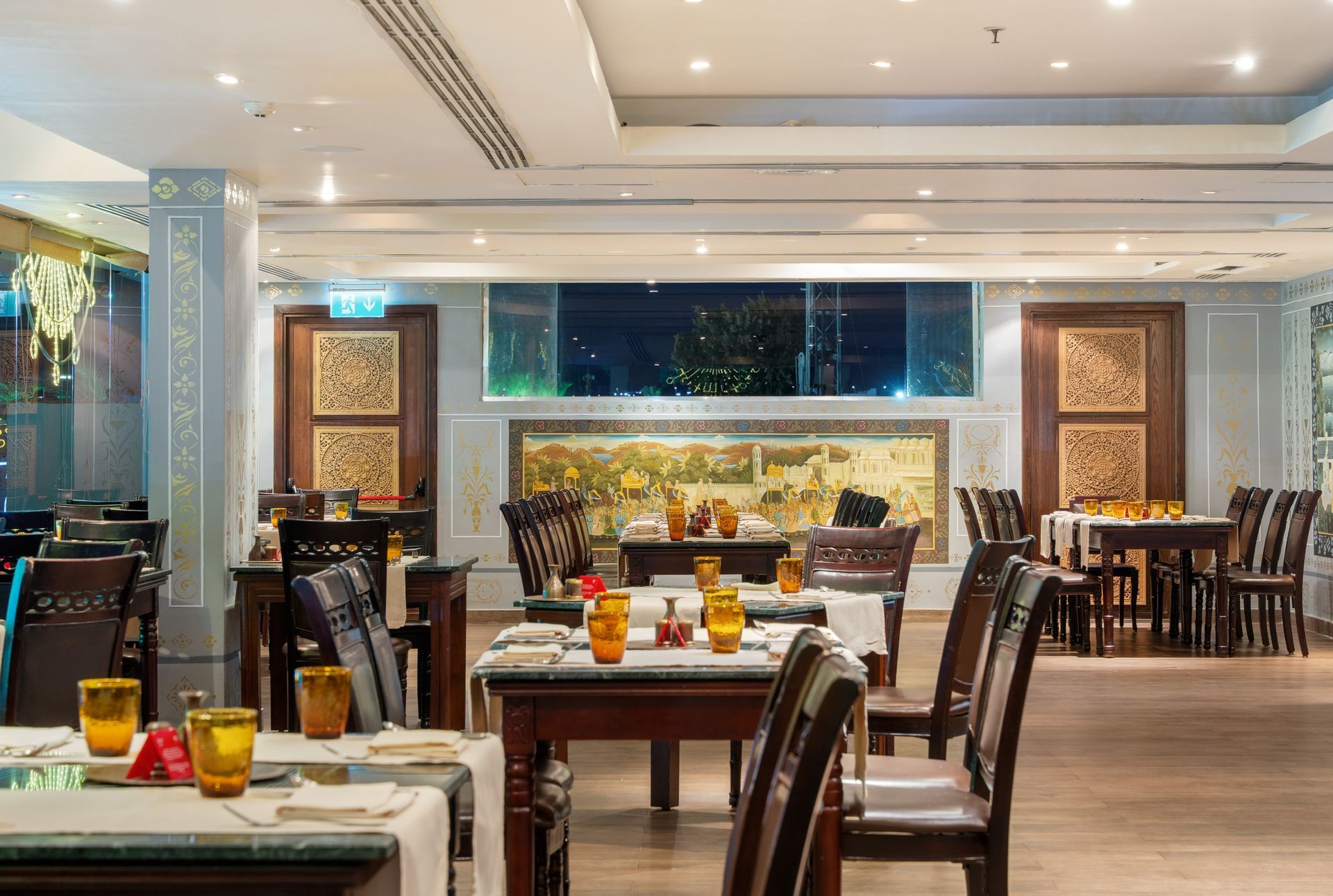 Restaurant interior with tables set for dining, ornate wooden chairs, and artwork.