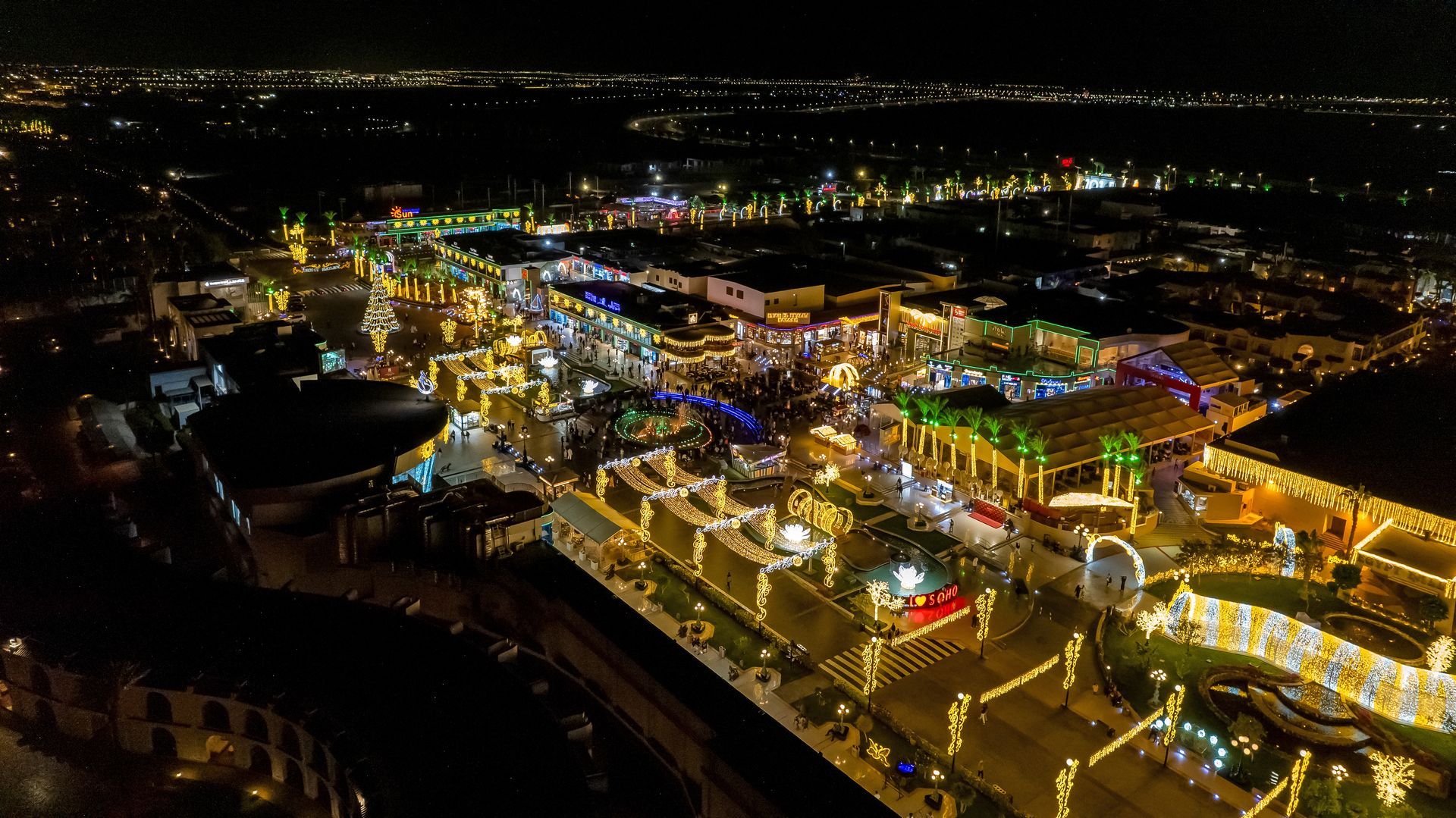 Aerial view of a brightly lit night market with many vendors, people, and festive lights.