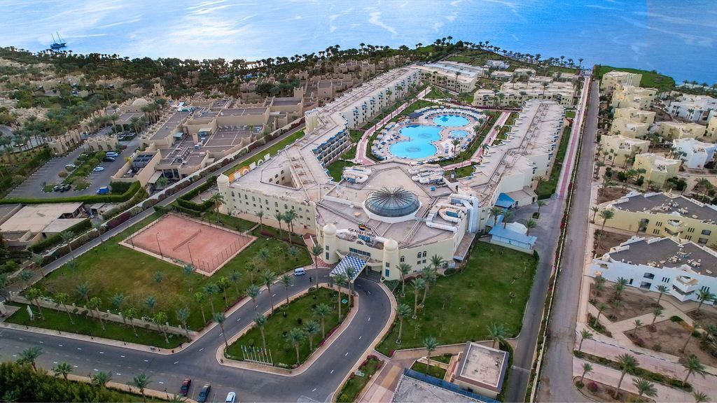 Aerial view of a large beige resort with pools, green lawns, and ocean access.