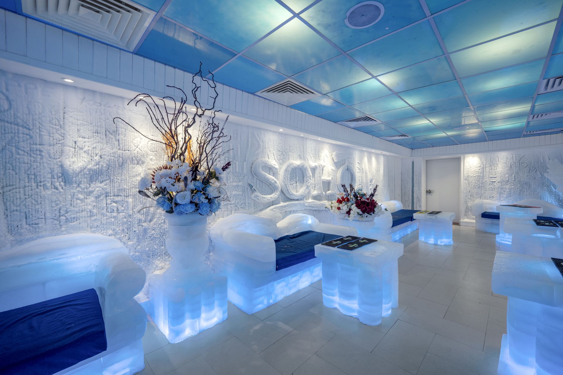 Ice lounge with ice furniture, blue lighting, and floral decorations.