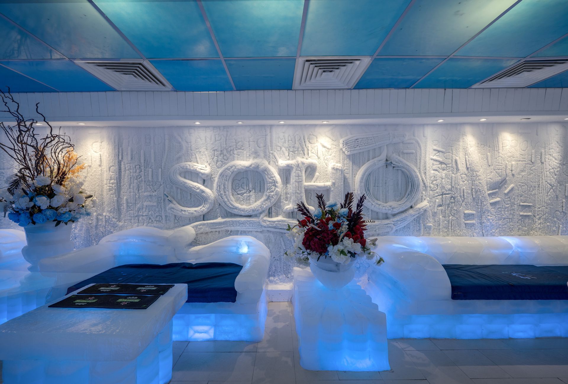 Ice lounge with ice furniture and SOHO carved in ice. Blue lighting and flowers.