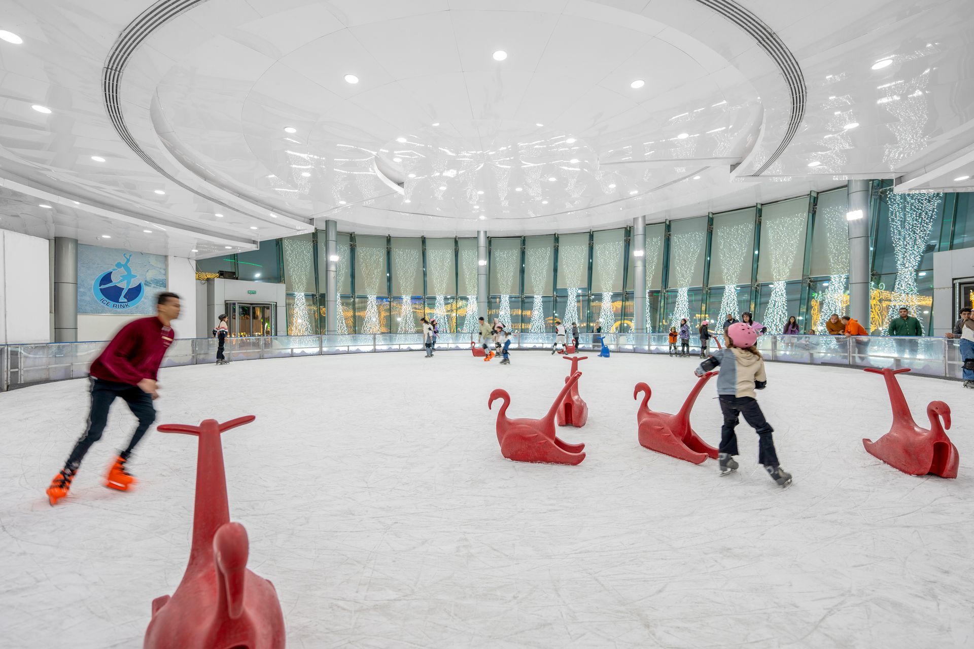 People ice skating in a circular rink with red animal-shaped skating aids.