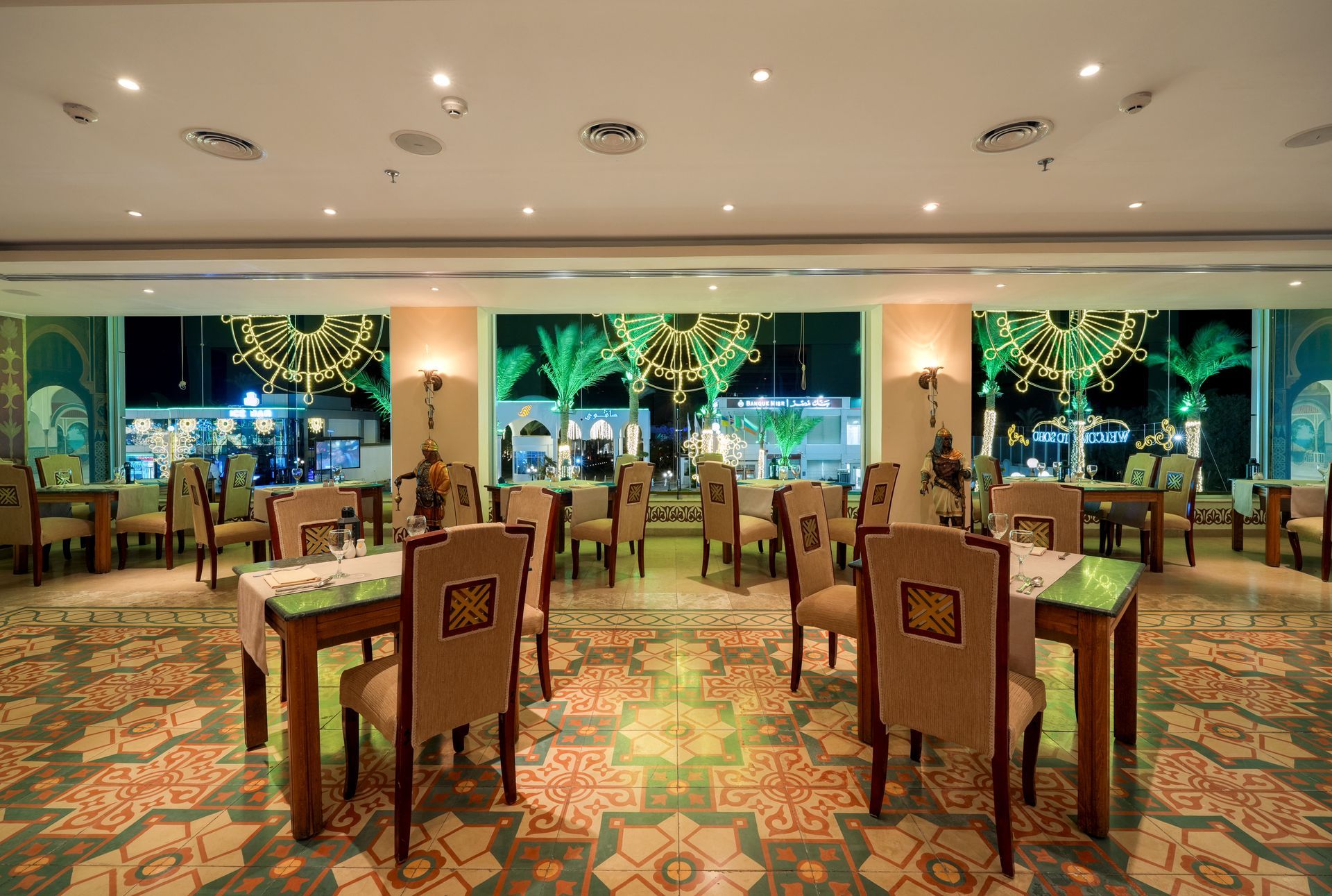 Restaurant interior with tables, chairs, and a view of illuminated trees outside.