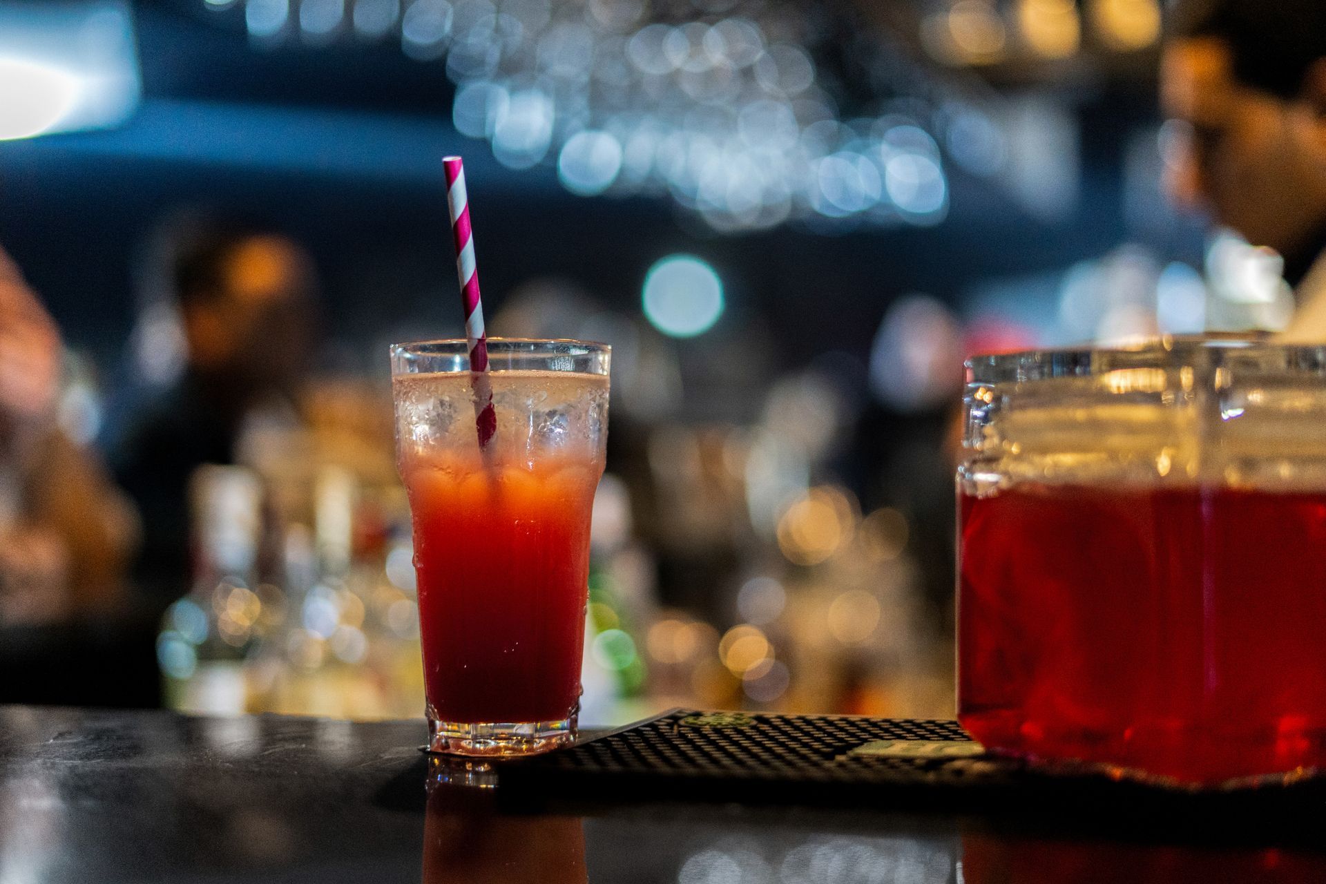 Cocktail with a striped straw on a bar in a dimly lit bar setting.