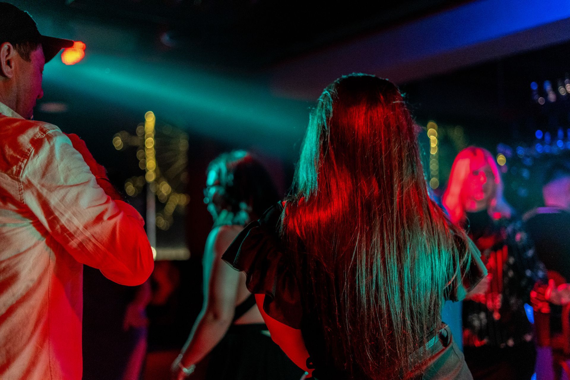People dancing in a club, with red and blue lighting. Woman in the center has long, dark hair.