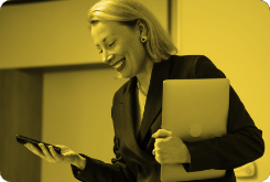 A woman in a suit is holding a laptop and a cell phone