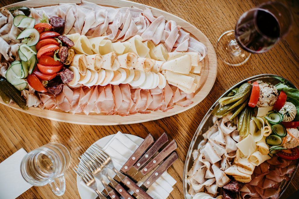 Wurst- und Käseplatten mit Fleisch, Käse und Gemüse, dazu ein Glas Wein und Besteck auf einem Holztisch.
