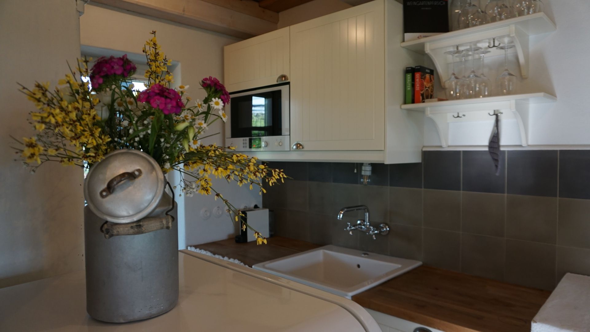 Küche mit weißen Schränken, Spüle und Blumen in einer Metallvase.